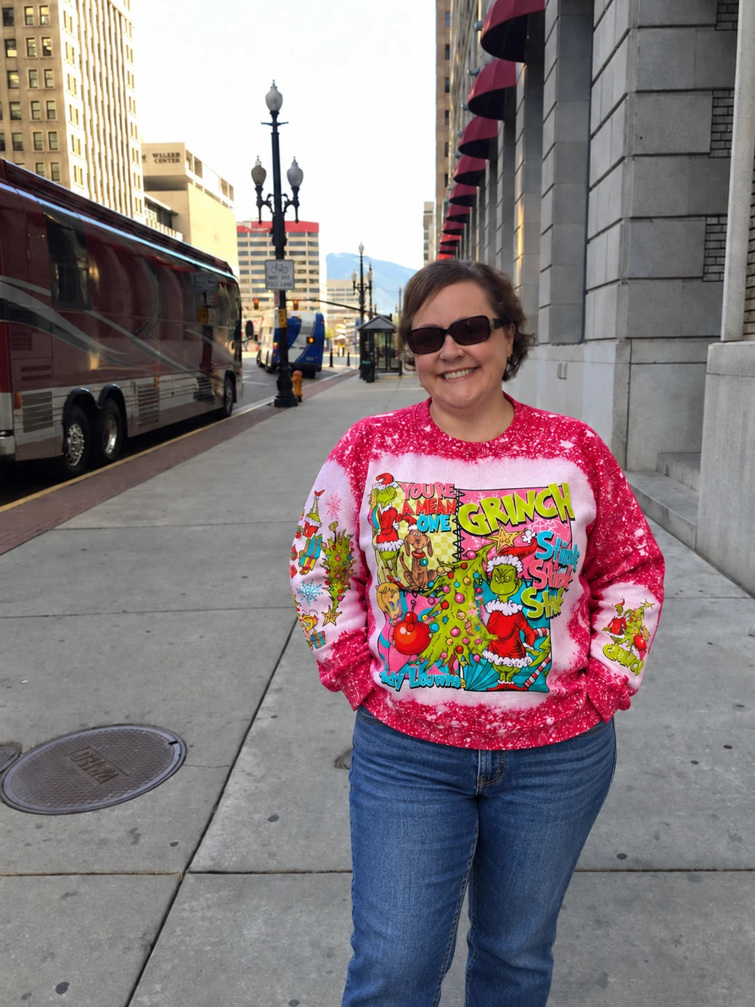Woman wearing the Mean One Green Guy Bleached Christmas Sweatshirt with jeans on a city sidewalk