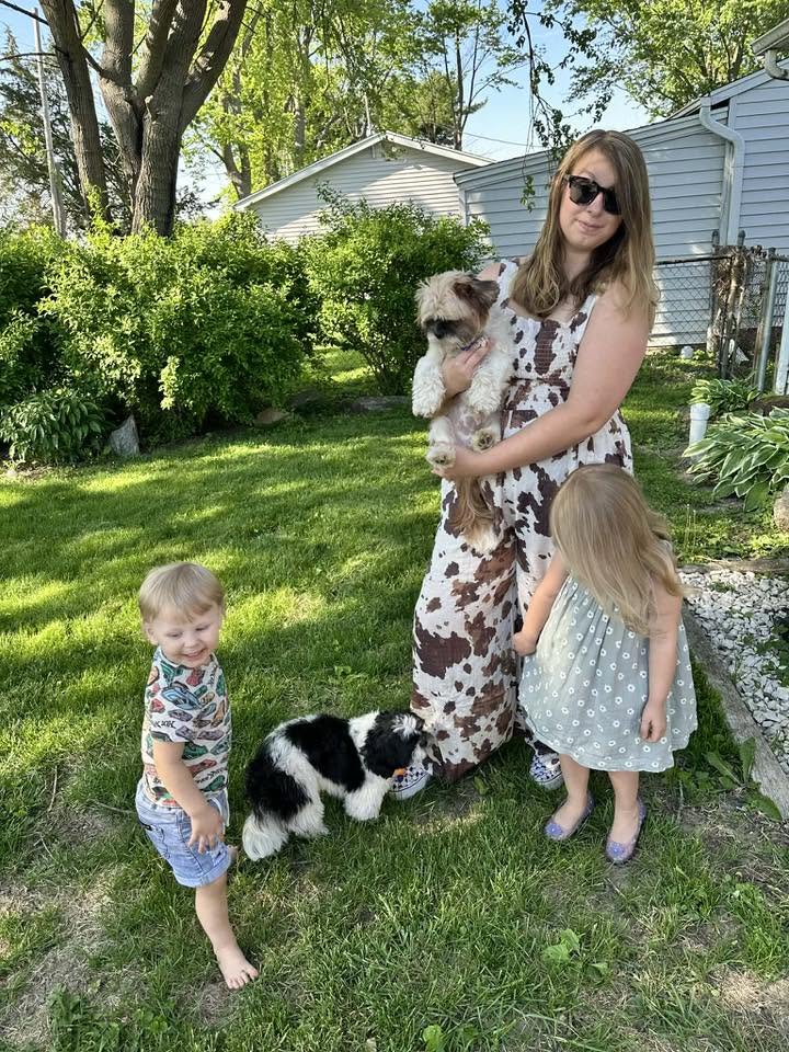 Woman wearing the Cow Camo Smocked Wide Leg Jumpsuit outdoors with two children and two dogs