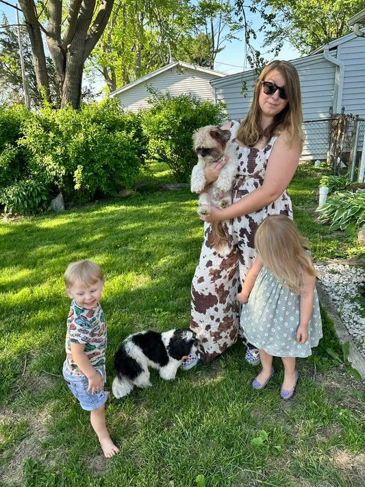 Woman wearing the Cow Camo Smocked Wide Leg Jumpsuit outdoors with two children and two dogs